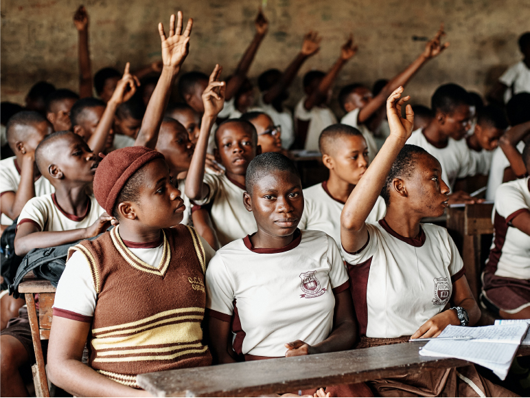 African school children raising their hands in class to answer a question.