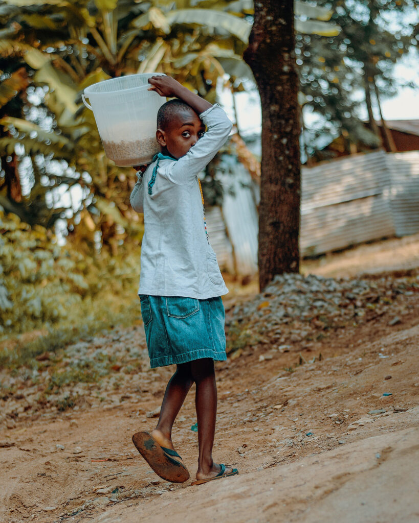Image of African child carrying bucket on shoulder.