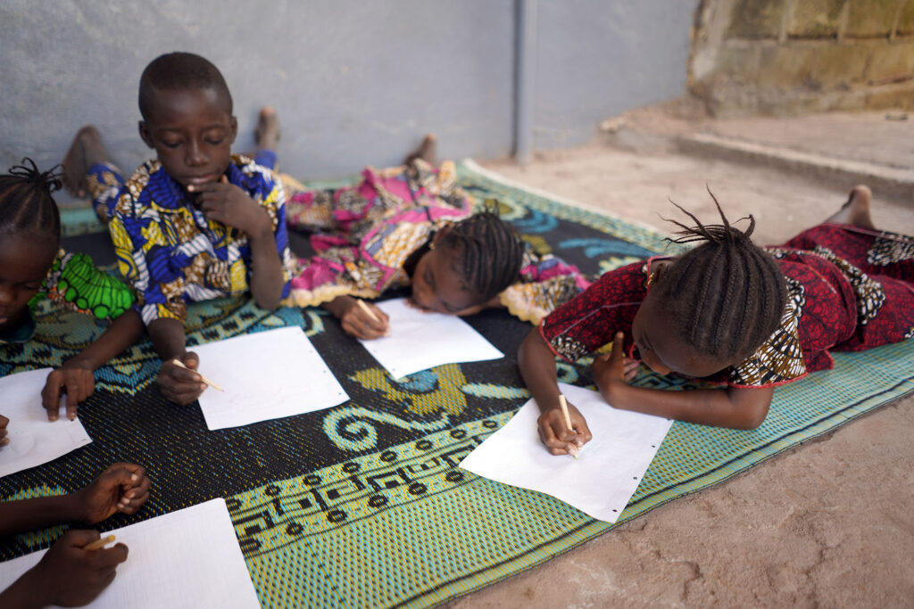 Image of 5 African children drawing or writing on a floor rug.